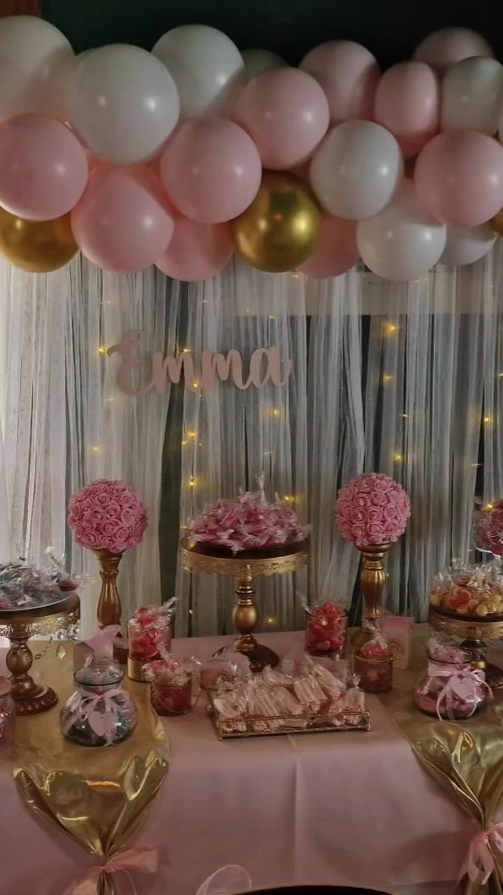 Mesa dulce de comunión con rosas, dulces y photocall con el nombre de la niña bajo un arco de globos