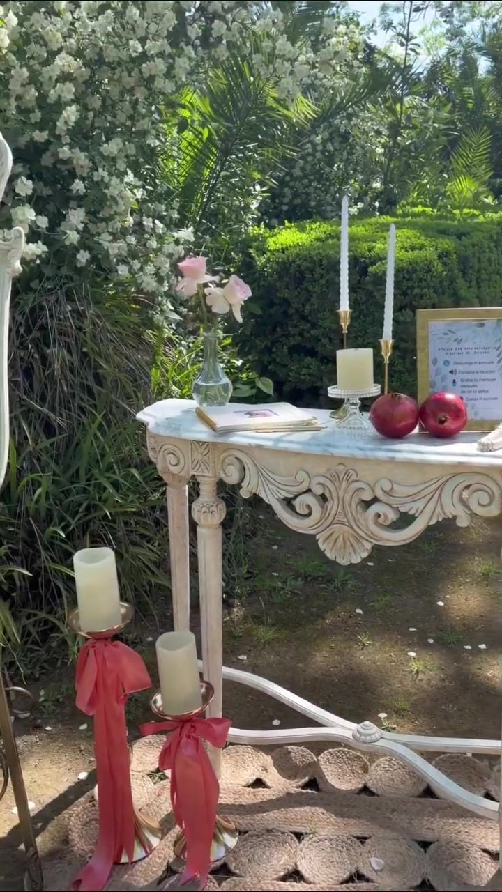Mesa de firmas con velas, lazos rojos y granadas bajo un arco floral