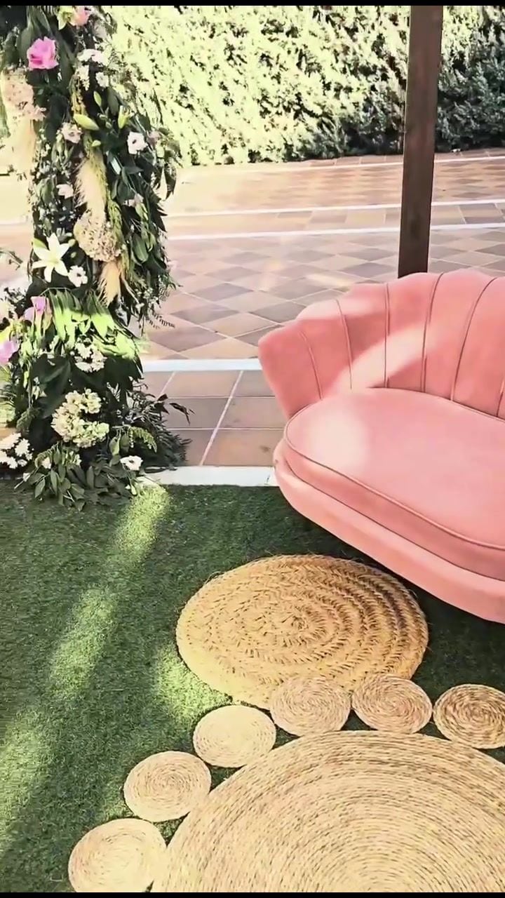 Sillón de terciopelo rosa sobre alfombra de yute en el jardín de la boda
