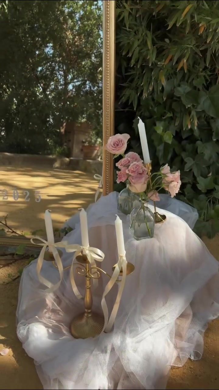 Velas blancas sobre mesa vestida con tul y rosas en un jardín